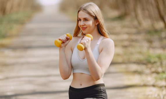 Fit woman lifting dumbbells on a sunny day, embracing a healthy outdoor workout.